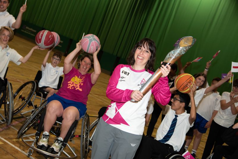 Felicity Amswych holding the Baton in front of Wheelchair Basketball players.